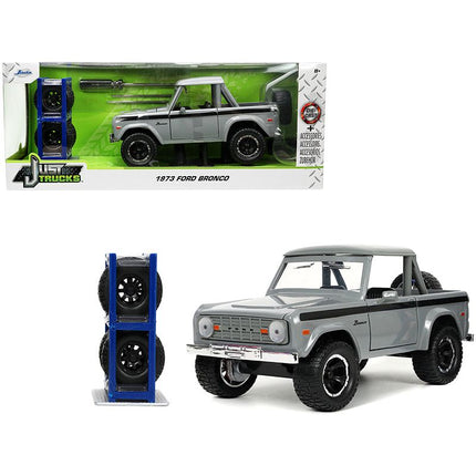 https://cdn.shopify.com/s/files/1/0504/9925/6496/files/1973-ford-bronco-pickup-truck-gray-with-black-stripes-with-extra-wheels-just-trucks-series-124-diecast-model-car-by-jada-835326.jpg?v=1748419223