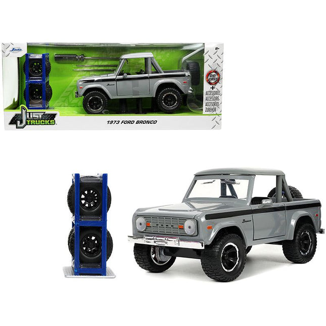 https://cdn.shopify.com/s/files/1/0504/9925/6496/files/1973-ford-bronco-pickup-truck-gray-with-black-stripes-with-extra-wheels-just-trucks-series-124-diecast-model-car-by-jada-835326.jpg?v=1748419223