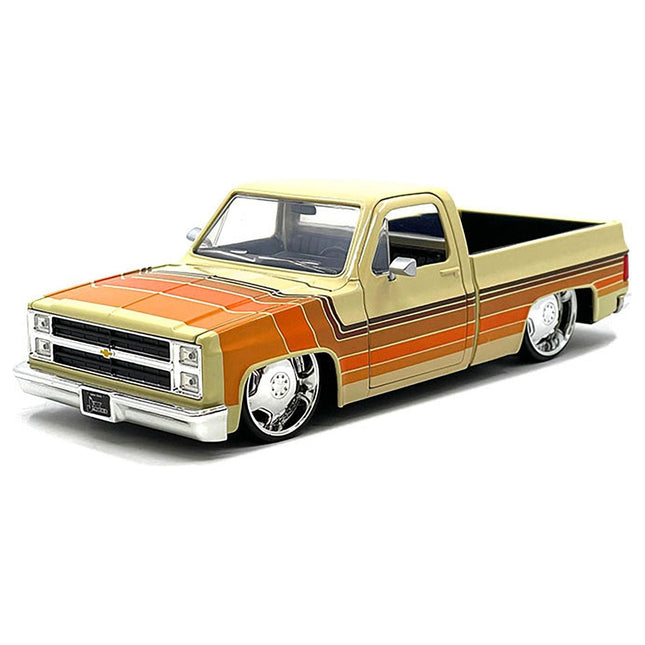 https://cdn.shopify.com/s/files/1/0504/9925/6496/files/1985-chevrolet-c-10-pickup-truck-beige-with-stripes-and-lowenhart-wheels-just-trucks-series-124-diecast-model-car-by-jada-693745.jpg?v=1748405107