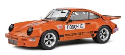 Orange Porsche diecast model car, classic racing design with Donohue decals, 1:18 scale.
