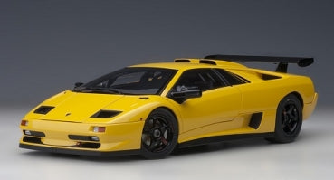 Yellow diecast model car in 1:18 scale, sports design with rear wing on a grey background.