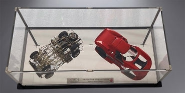 1:18 scale red diecast model car with exposed chassis and body displayed in a glass case