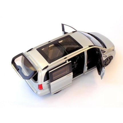 High-angle view of a 1:18 scale Mercedes-Benz V-Class (W447) AMG Line 2018 diecast model in brilliant silver metallic, showing the driver's front door and sliding passenger door open to reveal the beige interior. The long van body features a panoramic glass roof, roof rails, and multi-spoke wheels.