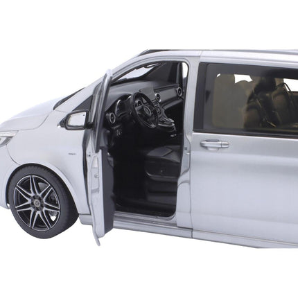 Close-up view of the driver's side of a 1:18 scale Mercedes-Benz V-Class (W447) AMG Line 2018 diecast model in brilliant silver metallic, showing the front door open to reveal the detailed beige interior with steering wheel and dashboard. The open sliding side door and multi-spoke wheel are also visible against a white background.