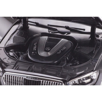 Close-up view of the engine bay on the 1:18 scale Mercedes-Maybach S 680 4Matic (X223) diecast model, revealing a detailed V12 engine cover and surrounding mechanical components under the open hood. The shot highlights the intricate engine detailing and chrome grille edge at the front.