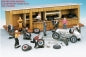 Diecast model car repair scene with figures, classic race car, tools, and wooden garage backdrop