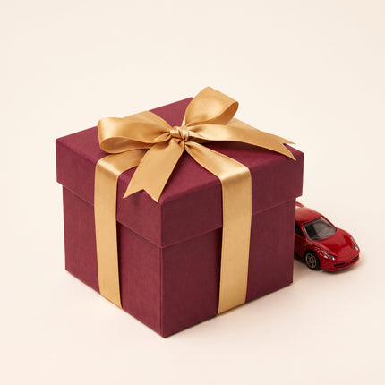 Gift wrapping in red paper with gold ribbon next to a model car