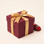 Gift wrapping in red paper with gold ribbon next to a model car